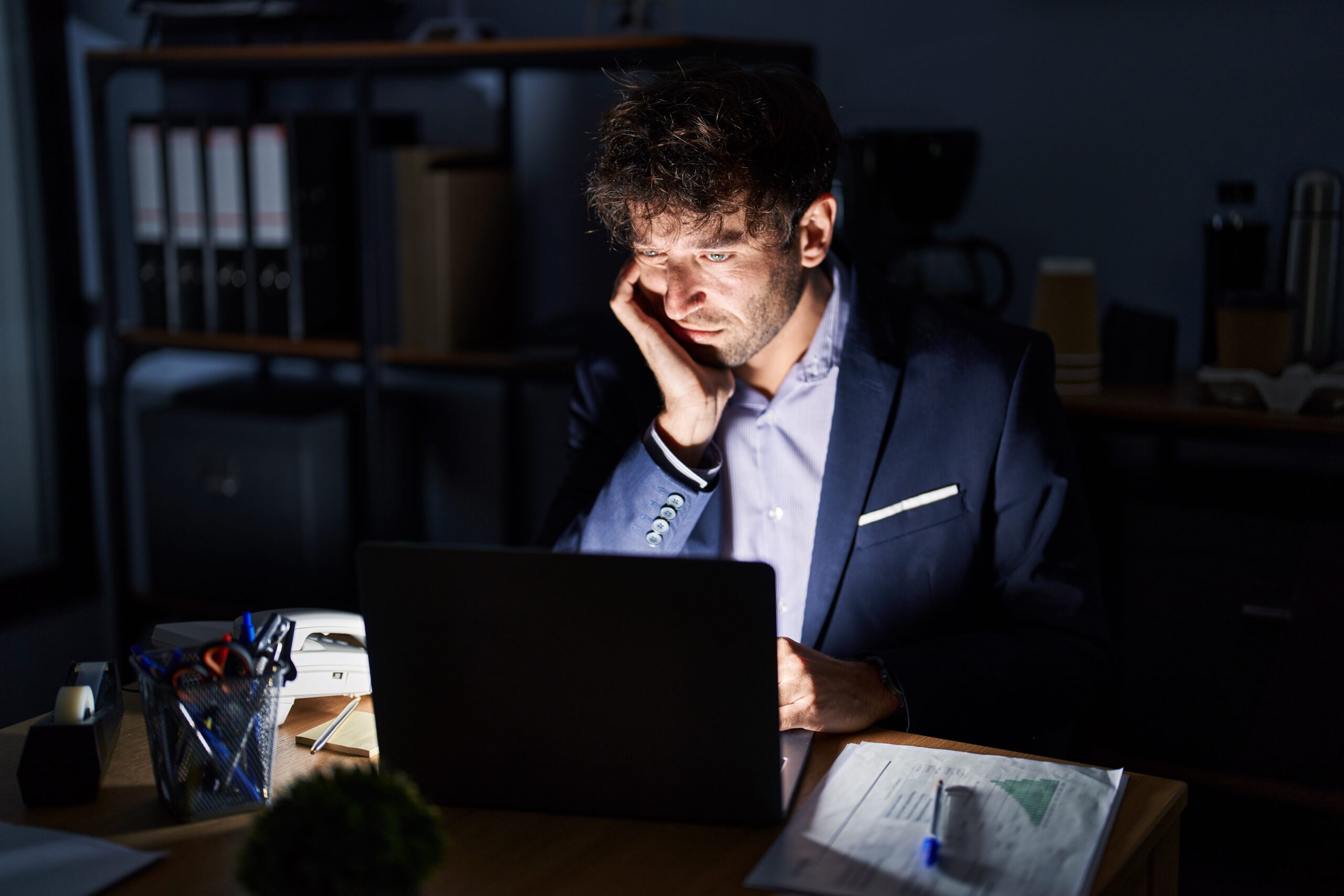Hispanic young man working at the office at night thinking looking tired and bored with depression problems with crossed arms - Bidaya Global